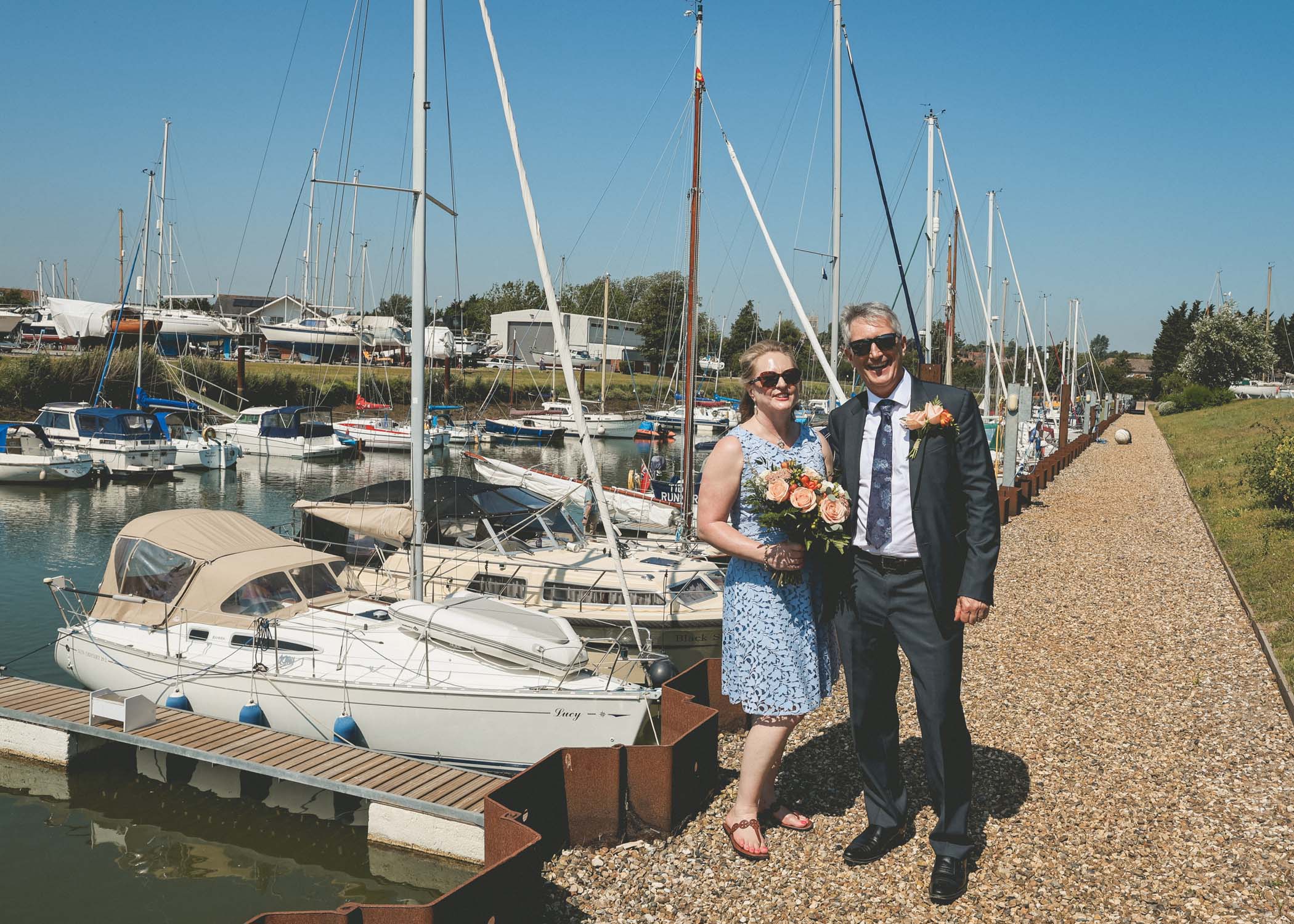A bride and groom stood in front of their boat in woodbridge marina on a wedding day in Woodbridge captured by Suffolk Wedding Photographer Hayley Denston Photography